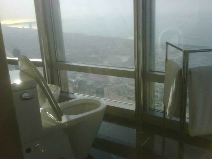 Toilet with open lid in a high-rise bathroom offering a panoramic city view captured for curious minds.