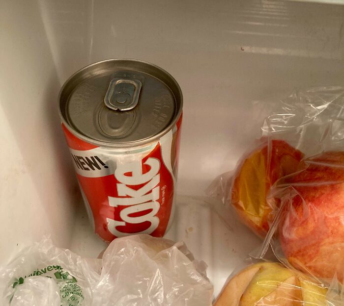Old can of Coca-Cola stored in a fridge alongside plastic bags and fruit, illustrating bizarre things found in old houses.