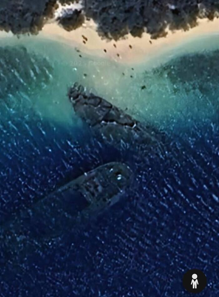 Aerial view of a shipwreck visible underwater near a forested coastline on Google Earth.