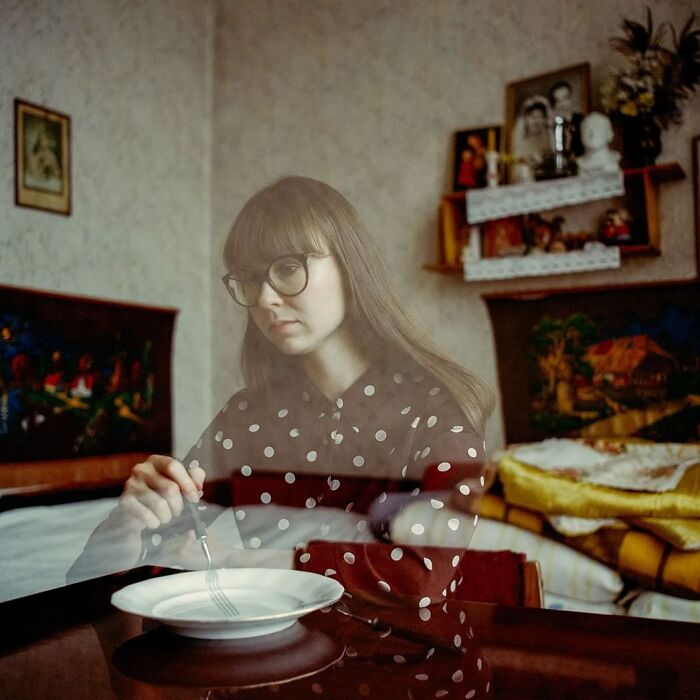 Young woman in vintage-style room holding a fork, captured in an intimate, cinematic-looking photograph with vintage cameras.