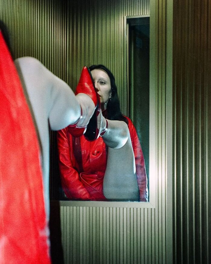 Woman in red leather jacket and shoes posing inside vintage-styled room for intimate cinematic-looking shot by photographer.