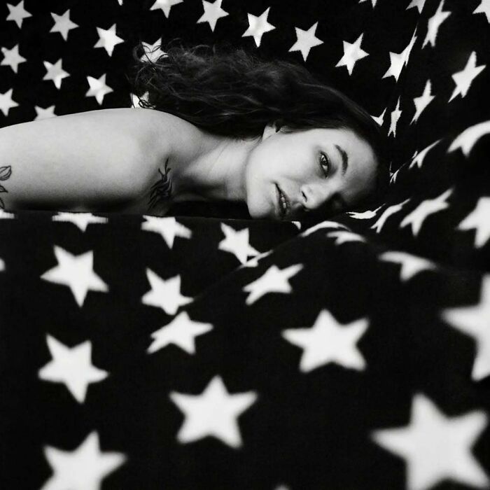 Black and white intimate shot of a woman lying on star-patterned fabric, captured with vintage cameras for a cinematic look.