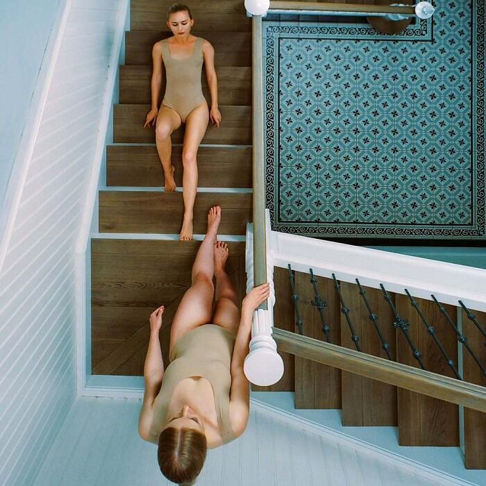 Two women in beige leotards captured using vintage cameras, posing on a wooden staircase for intimate cinematic shots.