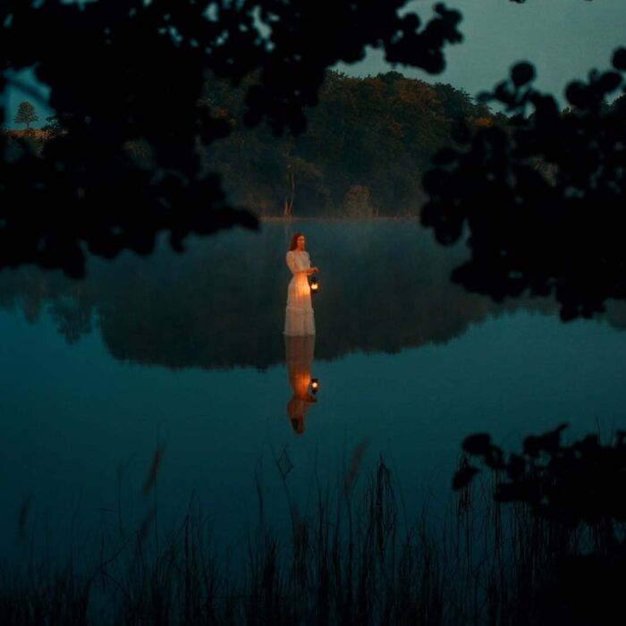 Photographer captures intimate, cinematic-looking shot of a woman in white holding a lantern, reflected on calm water at dusk.