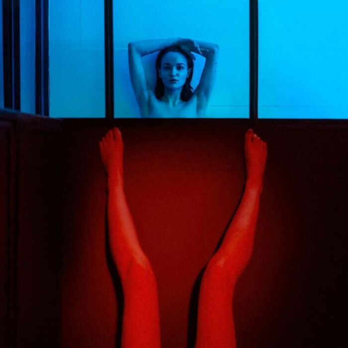 Woman posing with legs raised in a red-lit room, shot with vintage cameras to create intimate cinematic-looking photos.