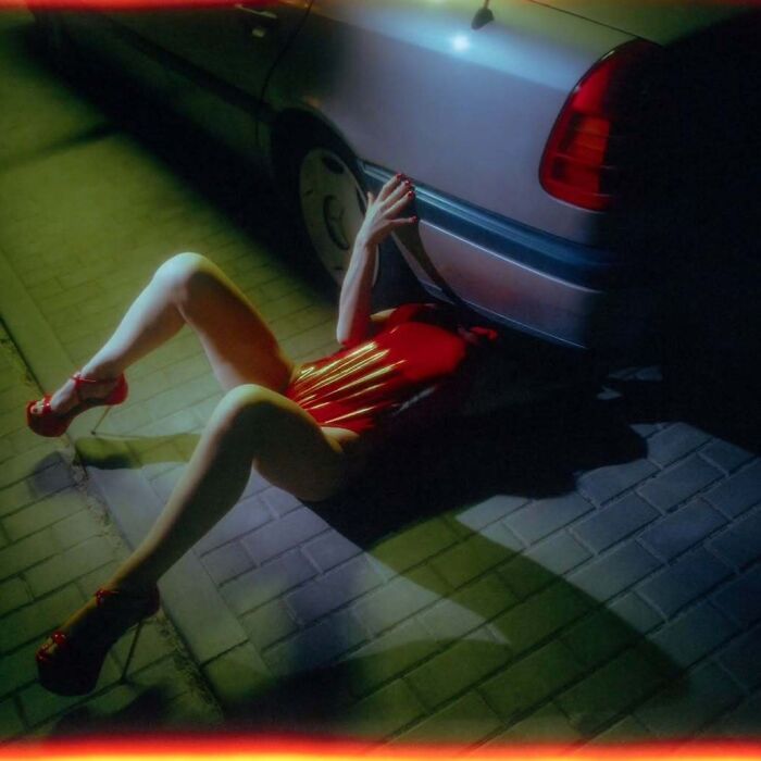 Person in red outfit lying on pavement beside a car, captured with vintage cameras creating intimate, cinematic-looking shots.