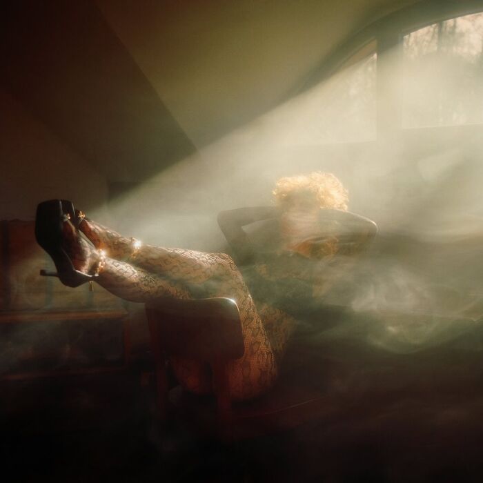 Woman reclining in chair with legs raised, bathed in soft light and mist, captured using vintage cameras for cinematic shots.