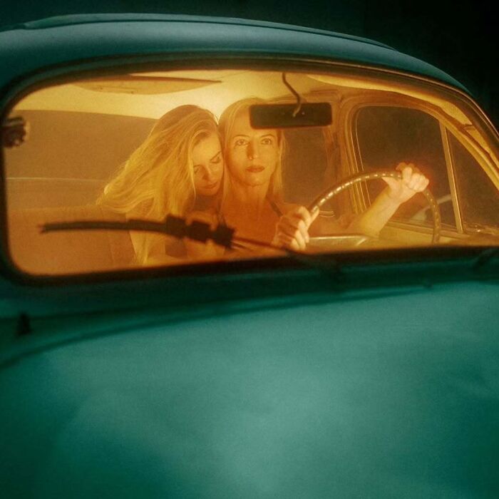 Two women in a vintage car captured with vintage cameras creating intimate, cinematic-looking shots in warm lighting.