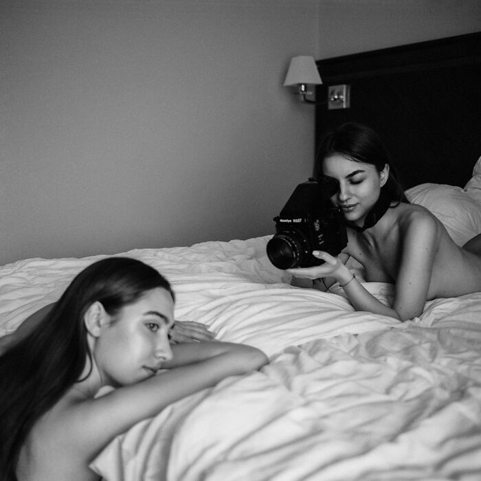 Two women on a bed using a vintage camera to capture intimate, cinematic-looking black and white shots in a cozy room.