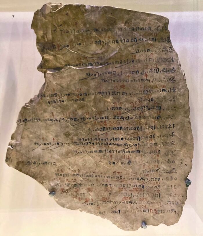 Ancient manuscript fragment with faded script displayed as a bizarre historical artifact in a museum exhibit.
