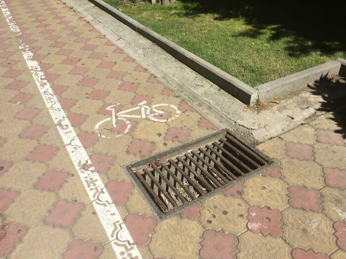 Bicycle lane intersecting with a dangerous metal grate posing a risk in hazardous designs and death traps.