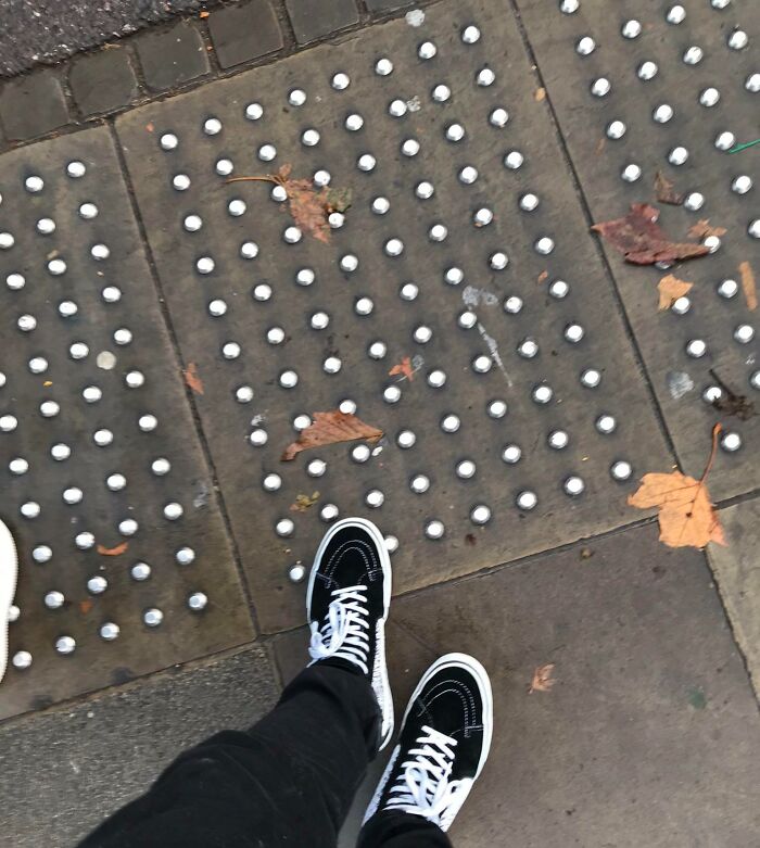 Person wearing black sneakers stepping on a pavement with raised tactile dots, illustrating dangerous design hazards.