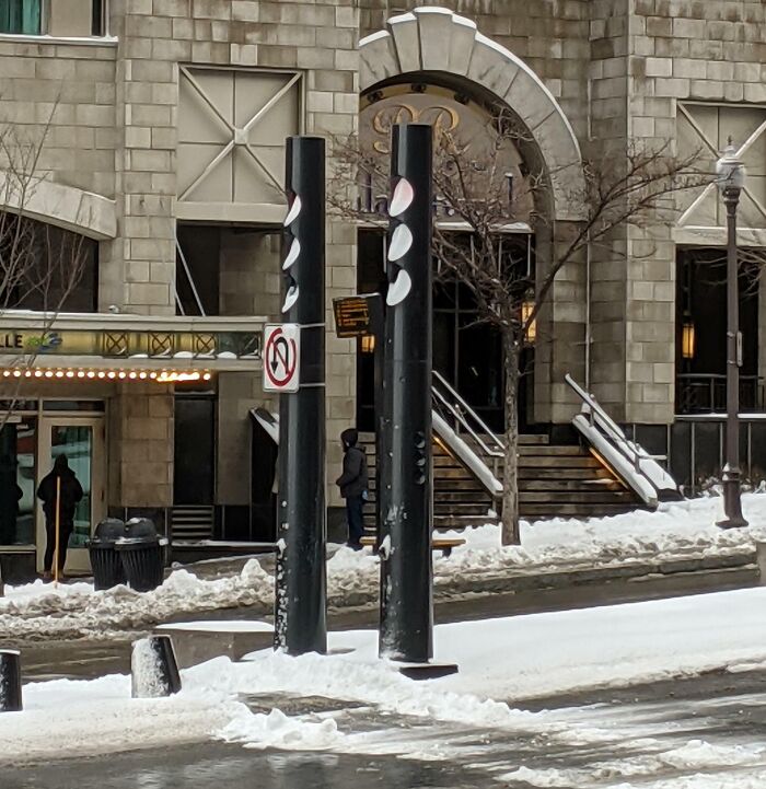 Street scene with snow and black poles blocking a no U-turn sign illustrating dangerous designs and death traps.