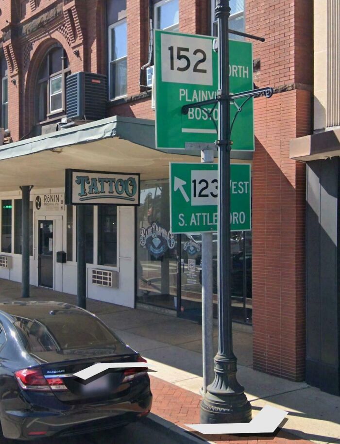 Street signs and a lamp post blocking the sidewalk next to a tattoo shop, an example of dangerous design death traps