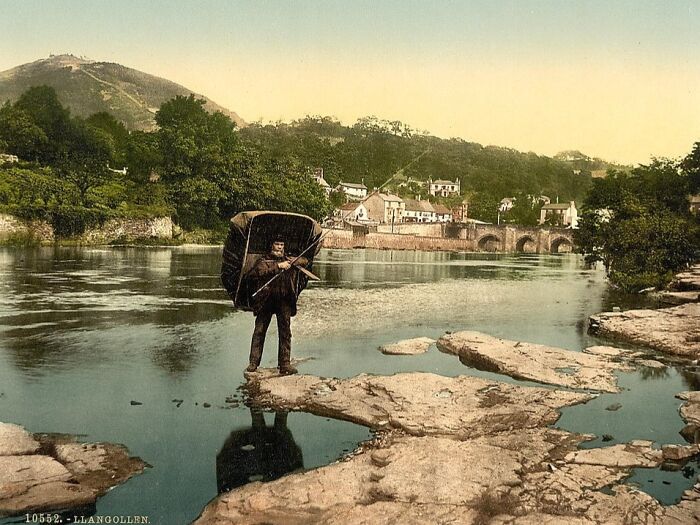 Man standing on rocks near river with umbrella in colorized photo revealing vibrant cultural past.