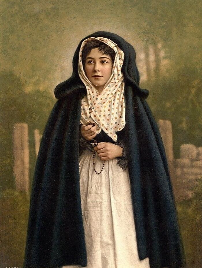 Young woman in traditional attire holding a rosary, showcasing vibrant cultural past in a colorized historical photo.