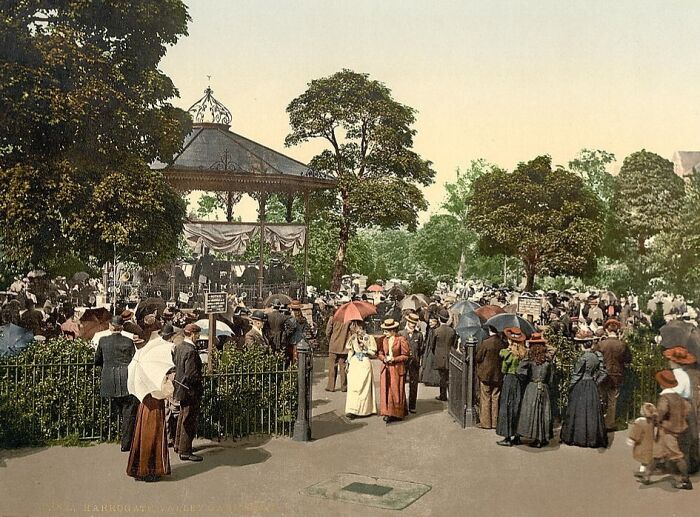 Crowd gathered in a park near a bandstand, showcasing a vibrant cultural past in a colorized historical photo.