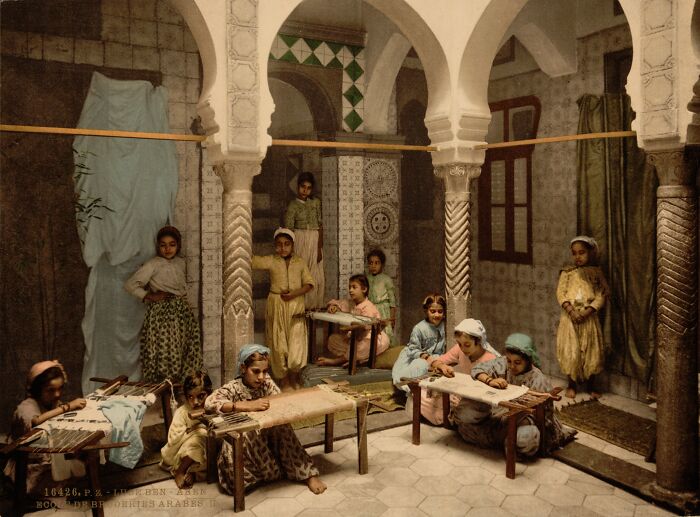 Group of children dressed in traditional clothes engaged in crafts inside a historic building, showing vibrant cultural past.