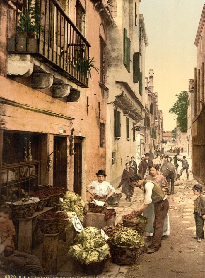 Colorized photo of a vibrant street market scene with people and baskets of vegetables in the cultural past.
