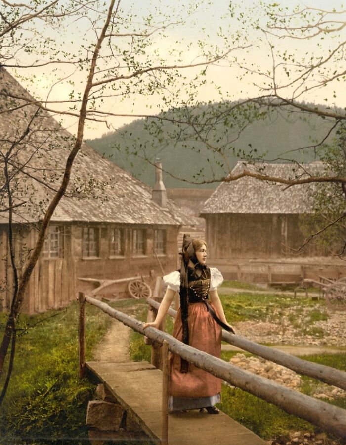 Young woman in traditional dress standing on a wooden bridge in a colorized photo revealing cultural past.
