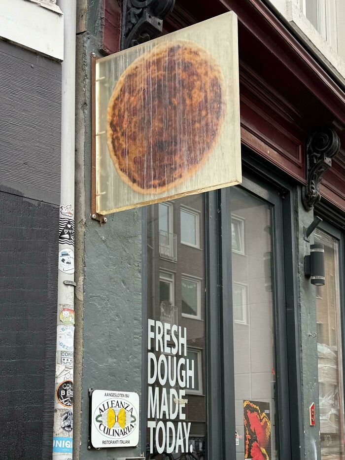 Sign outside an Italian restaurant with fresh dough made today text and a faded pizza image for curious minds.