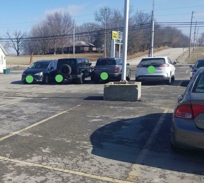 Cars parked dangerously close to a concrete barrier and pole in a flawed parking lot design causing safety hazards.