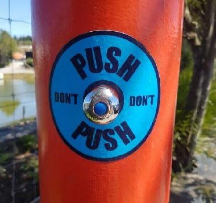 Blue push button on orange pole with confusing dangerous design featuring contradictory push and don’t push instructions outdoors
