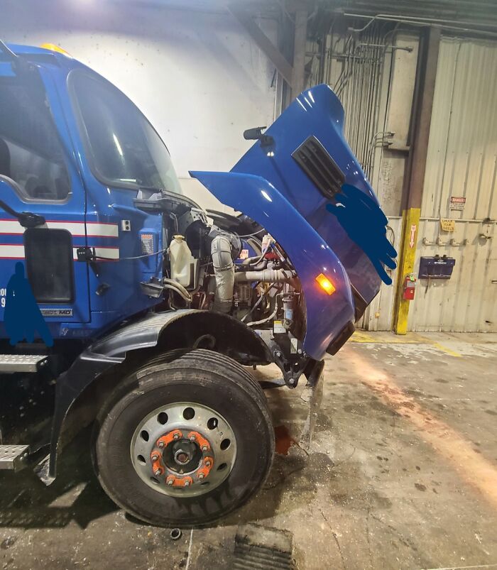 Blue semi truck with hood open inside industrial garage showing dangerous design death traps features.