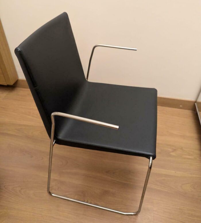 Black chair with metal frame and incomplete armrests, a dangerous design that could be classified as a death trap on wooden floor.
