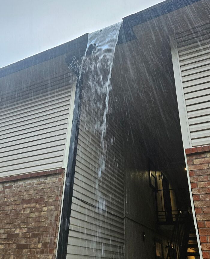 Water overflowing and falling unsafely from a building gutter in a dangerous design risk of death traps.