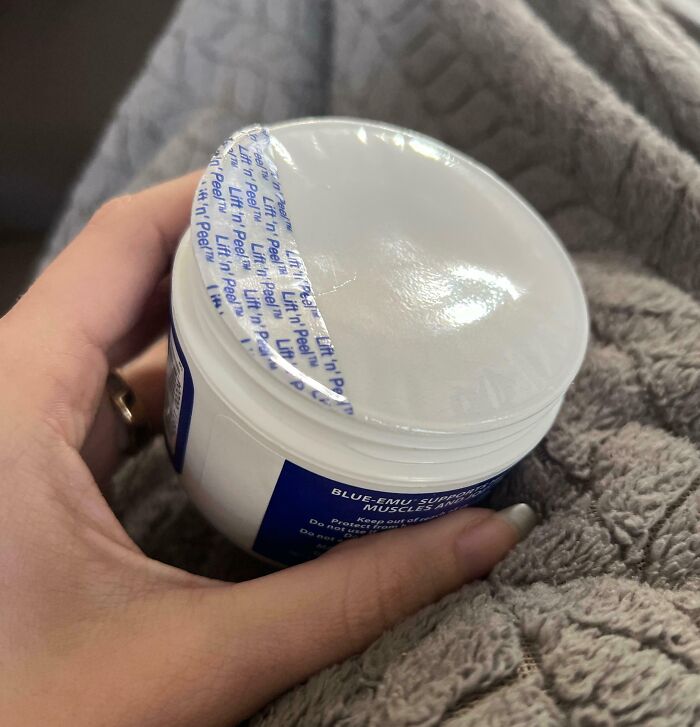 Hand holding a partially opened sealed container on a textured fabric, illustrating dangerous design concepts.