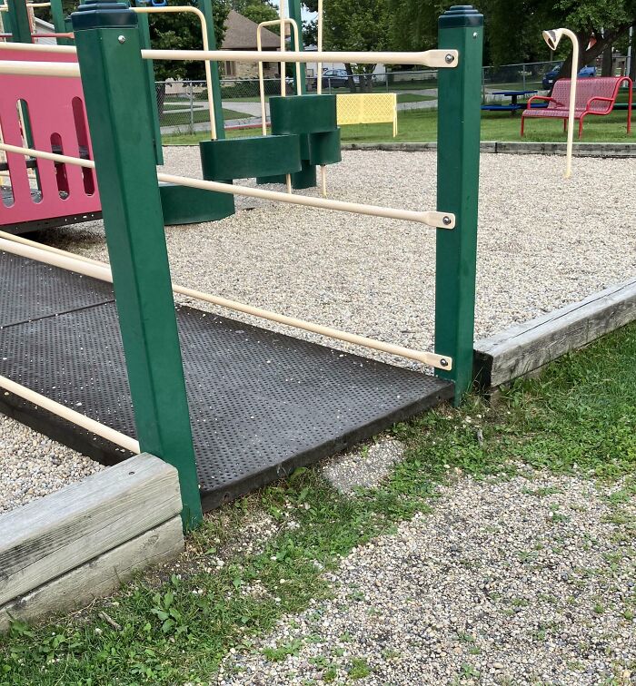 Playground ramp with missing edge guard creating a dangerous design hazard near gravel and grass surface.