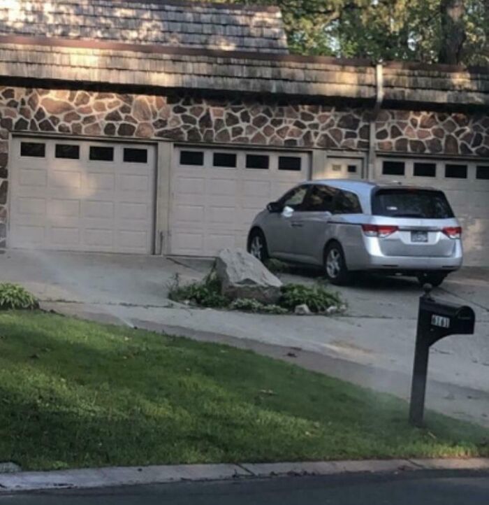 Driveway with a large rock blocking access to garage doors, an example of dangerous designs and death traps in architecture.