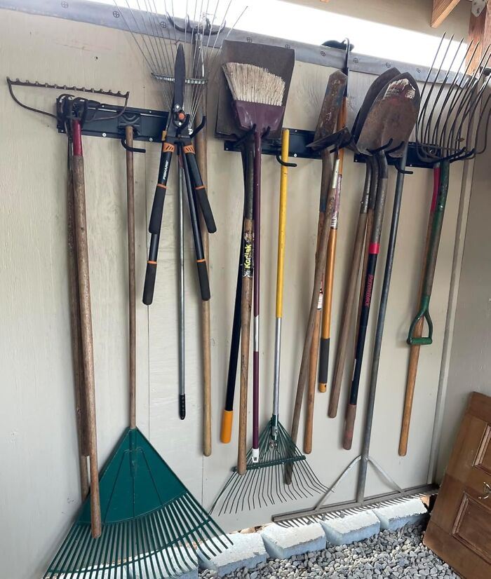 Various garden tools including rakes, shovels, and shears neatly hung and organized against a wall for easy access in a garden shed.