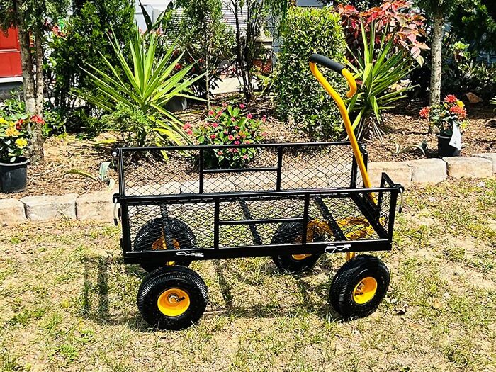 Black garden cart with yellow handle and wheels on grass in a backyard, representing garden's tiny tantrums solutions.