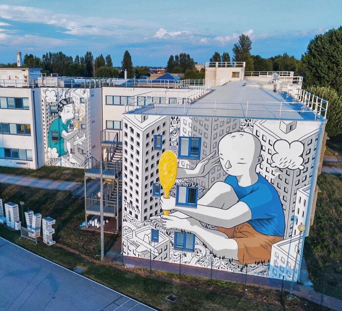 Large mural on city building by Italian artist depicting whimsical figure holding a yellow balloon in urban setting.