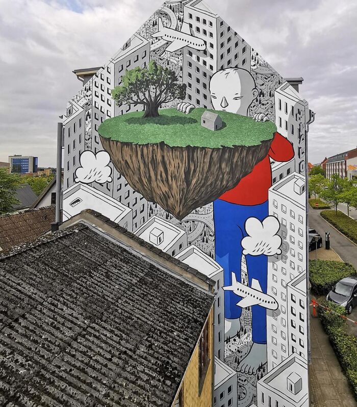 Italian artist mural shows whimsical cityscape with giant figure holding floating island on a colorful building wall outdoors.