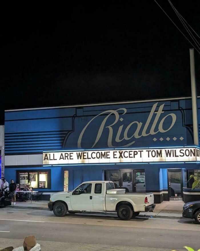 The Rialto theater at night with a marquee humorously excluding Tom Wilson, capturing main character moments in a hilarious way.