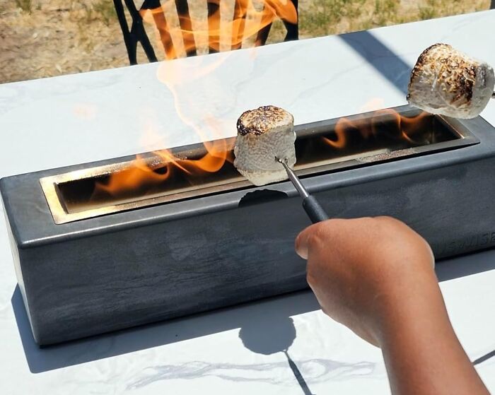 Hand roasting marshmallows over a modern tabletop fire pit, a perfect Father's Day finds gift idea.
