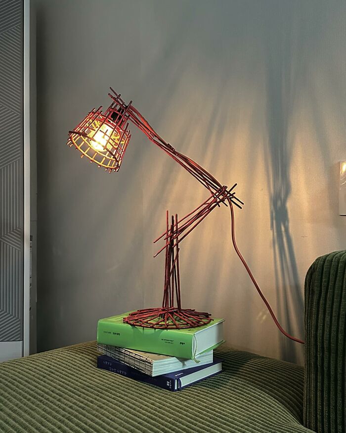 Red wire lamp designed to resemble a doodle placed on stacked books on a green corduroy sofa.