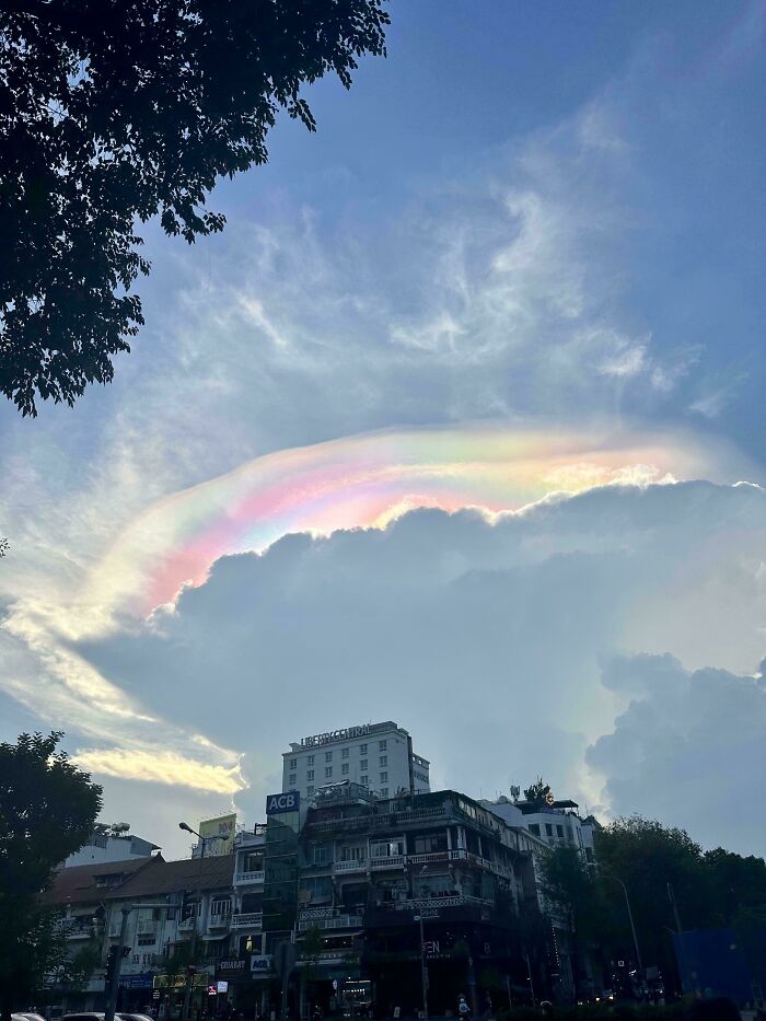 Rainbow-colored iridescent cloud above urban buildings, showcasing rare natural phenomena in the sky.