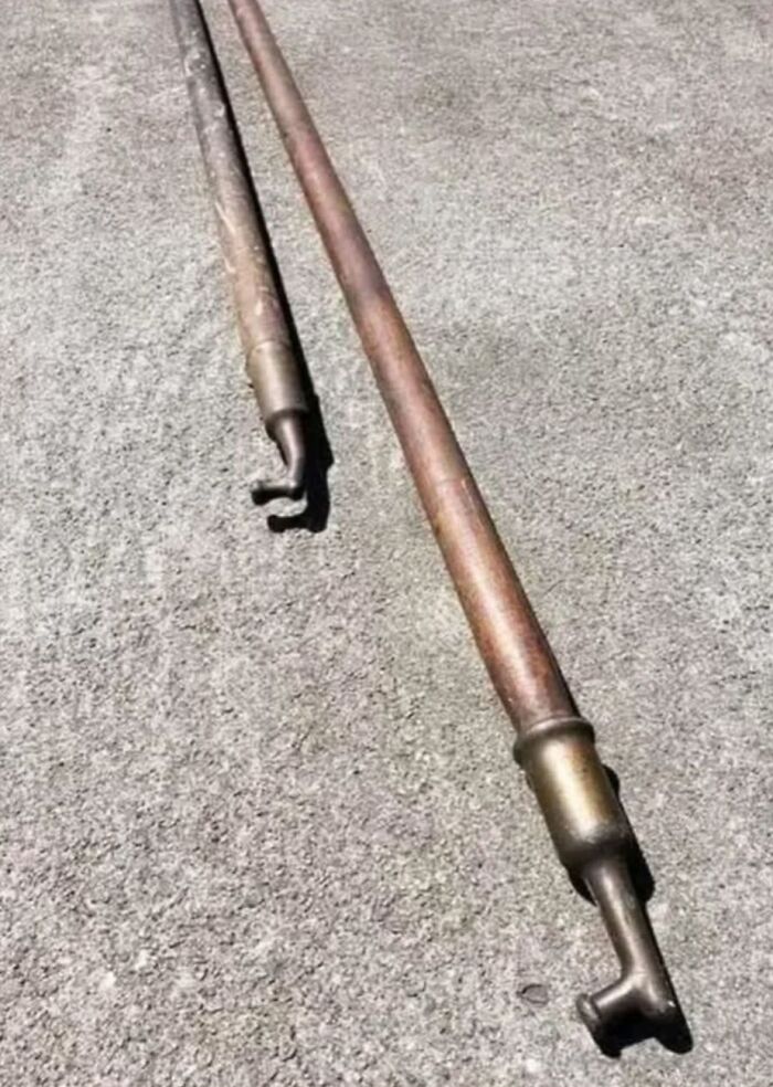 Two long rusty metal pipes with hooked ends lying on a rough concrete surface, strange things found in homes.