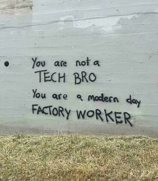 Graffiti on a wall stating a critique of modern work, reflecting themes of capitalism and labor in society.