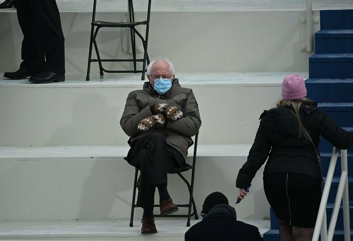 Older man wearing mittens and a face mask sitting alone on a folding chair, reflecting the exhaustion future doctors might feel.