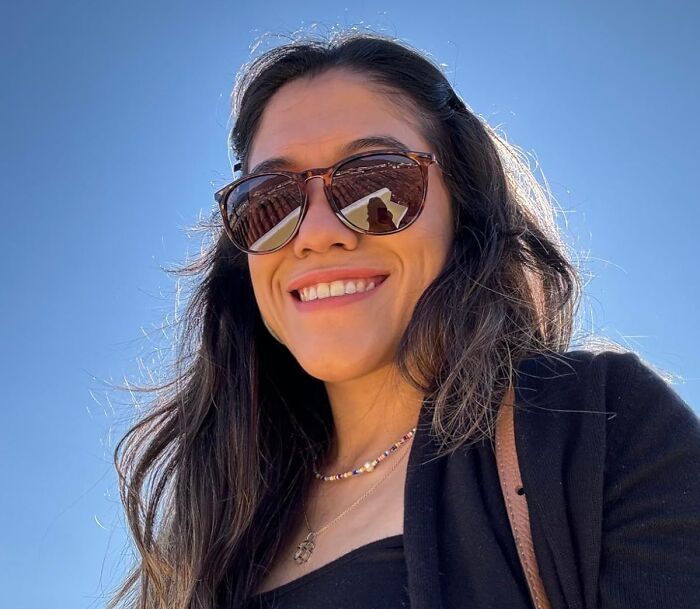 Smiling woman wearing sunglasses outdoors on a sunny day, showcasing a natural summer glow up look.