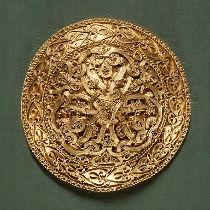 Intricately designed golden plate showcasing archeology and art with ornate patterns on a green fabric background