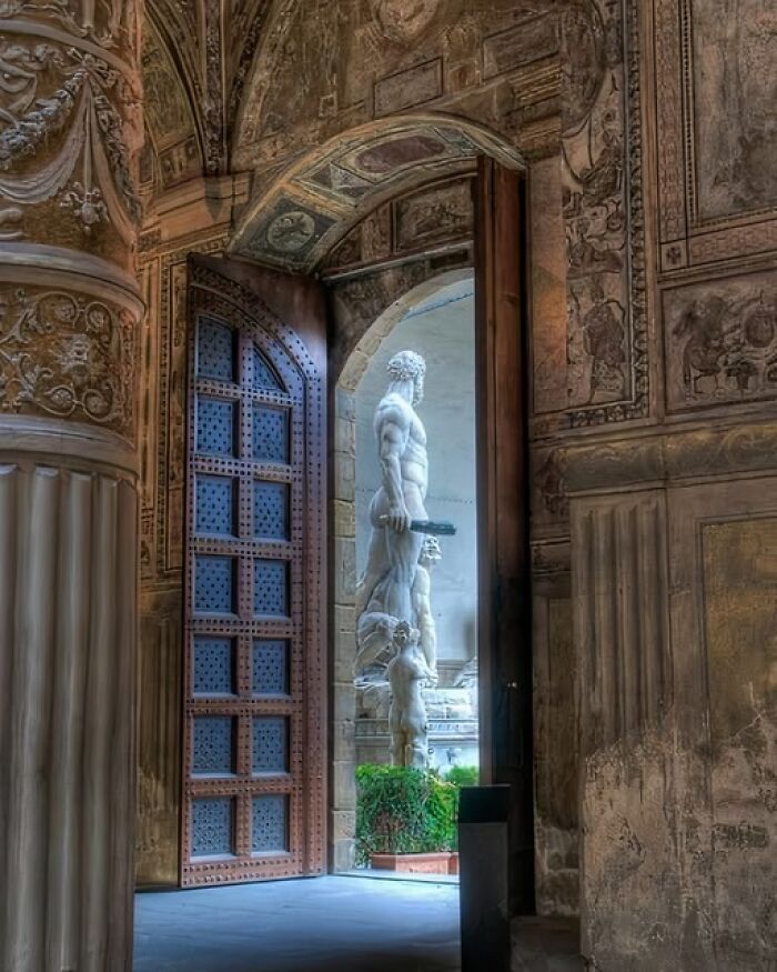 View of an ancient statue through an ornate door in a historic site showcasing archeology and art details.