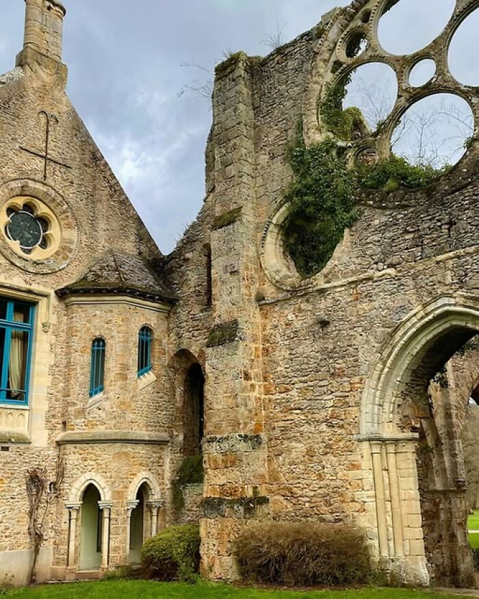 Ruins of an ancient stone building with arched windows and circular openings covered in moss and greenery.