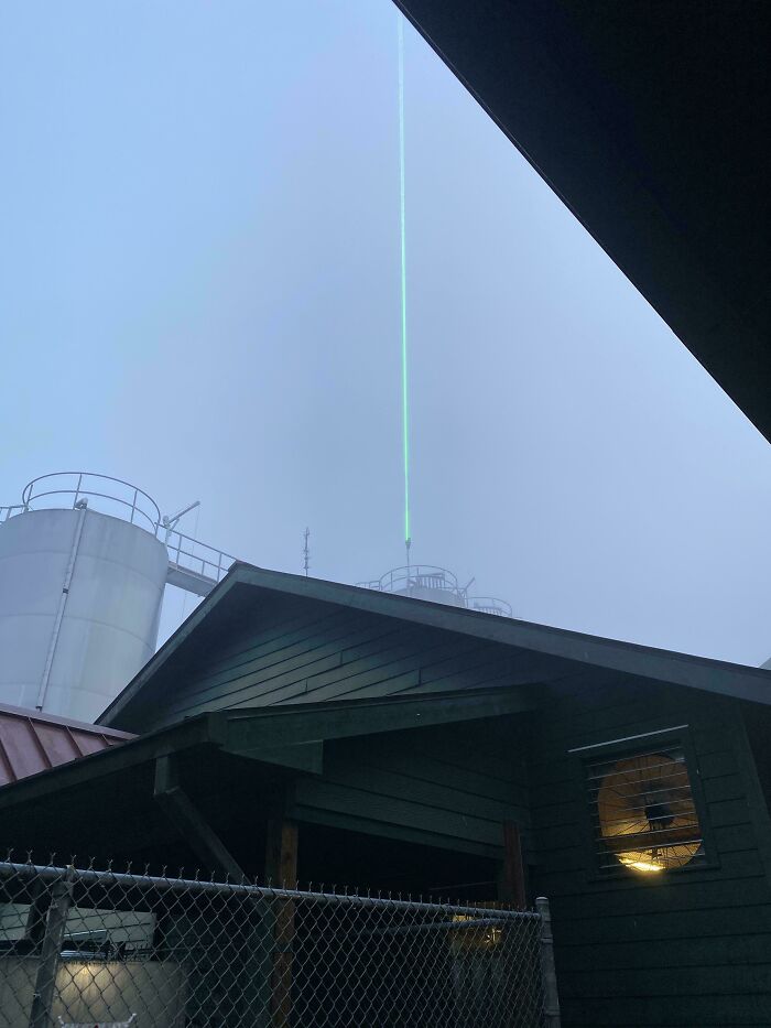 Green laser beam pointing skyward from rooftop against foggy sky, showcasing clever solutions to overlooked issues.