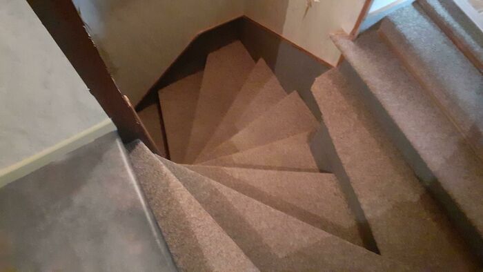 Carpeted spiral staircase with narrow steps and tight turn showcasing a dumb interior design decision.